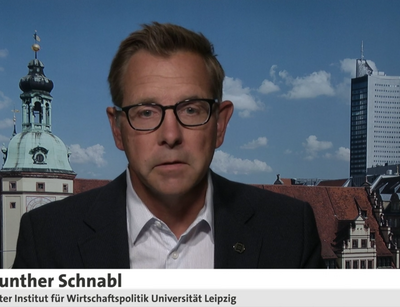 Standbild eines Fernsehbeitrags mit Günter Schnabl, Leiter des Instituts für Wirtschaftspolitik der Universität Leipzig, vor der Siluette Leipzigs