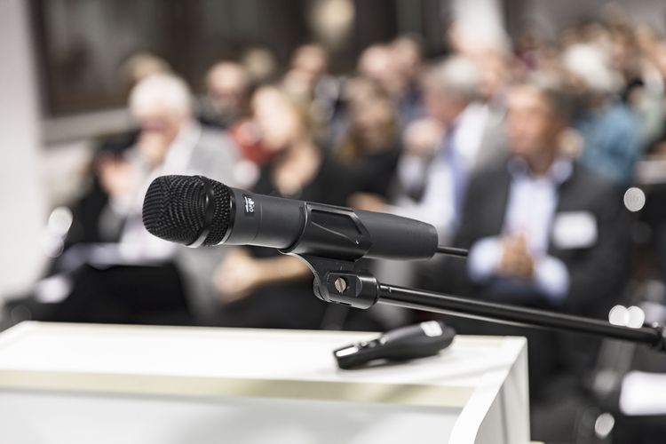 Foto eines Mikrofons an einem Rednerpult vor einem Publikum