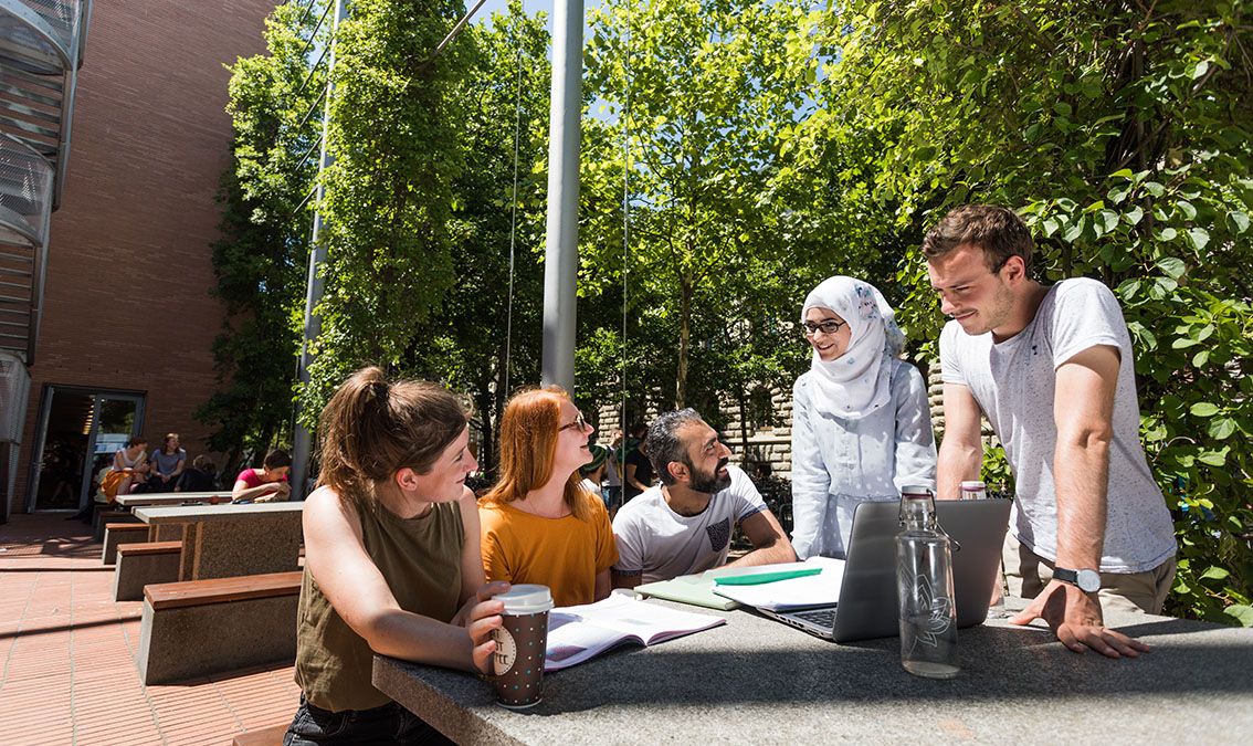 Studierende unterschiedlicher Herkunft unterhalten sich vor dem Geisteswissenschaftlichen Zentrum der Universität