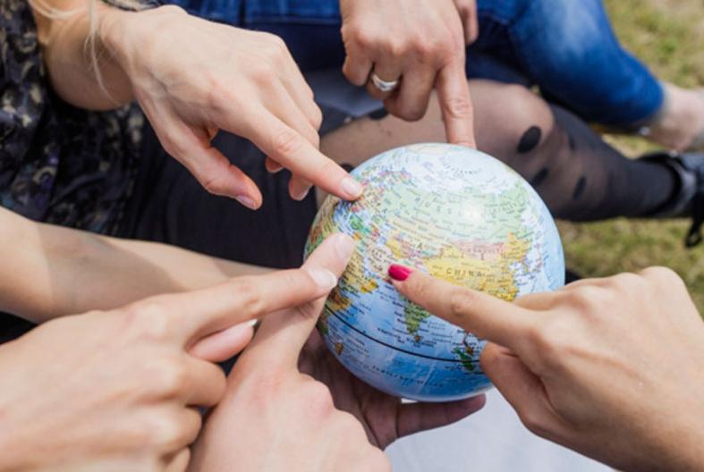 Foto: verschiedene Hände zeigen auf eine kleine Globuskugel